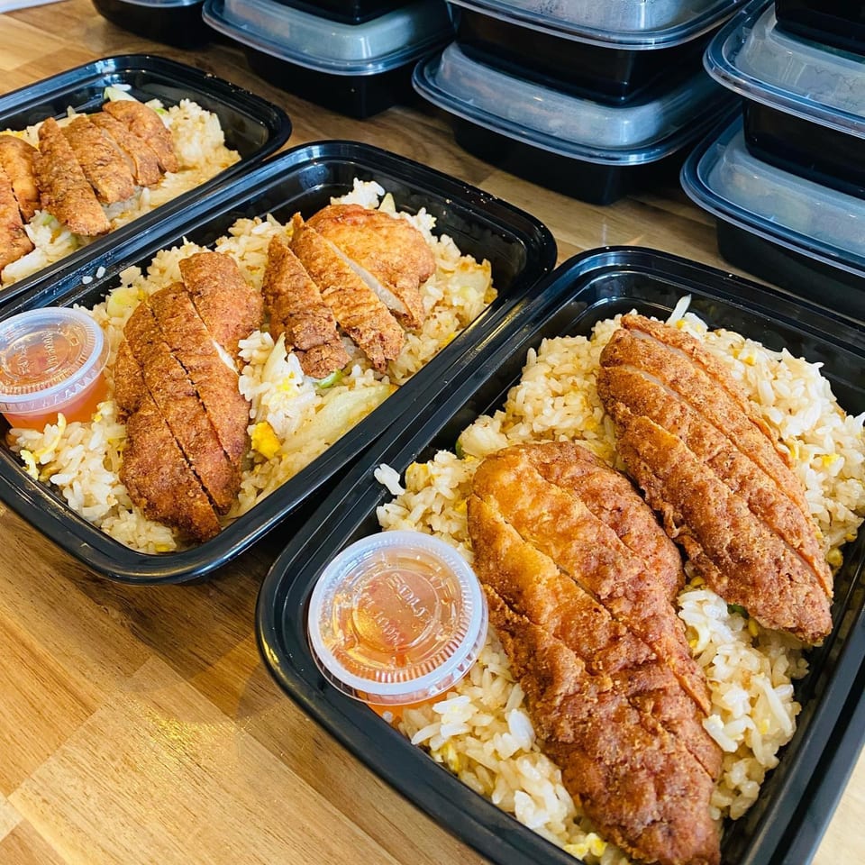 Multiple black containers of Thai fried chicken over rice with a side of sauce.