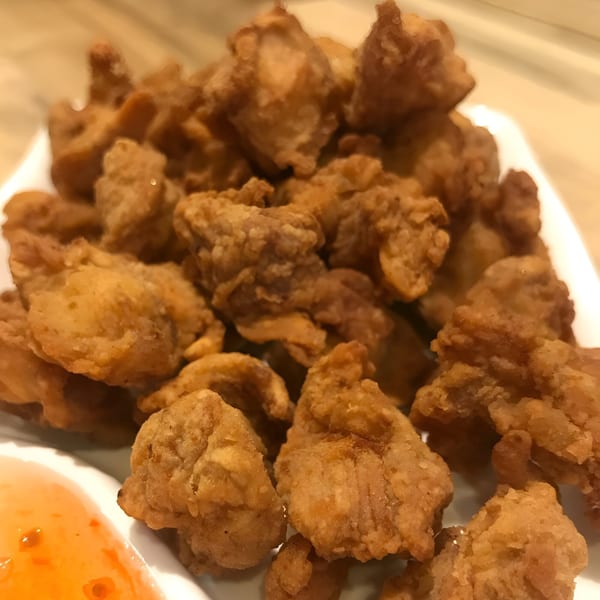Close-up of golden-brown fried chicken pieces on a white plate with a side of sweet chili sauce.