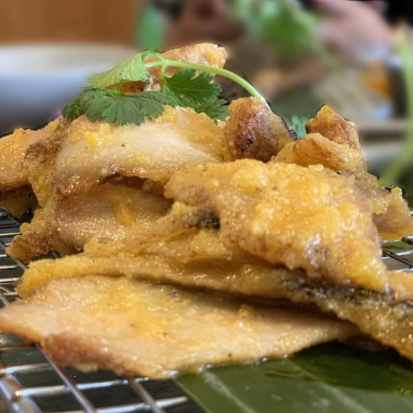 Crispy fried pork belly slices with cilantro garnish, served on a metal rack over a banana leaf.