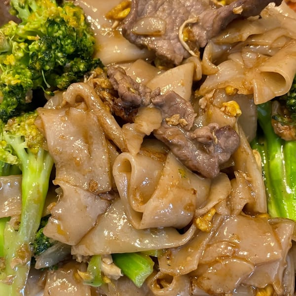 Close-up of Thai Pad See Ew with wide rice noodles, beef, broccoli, and scrambled egg.