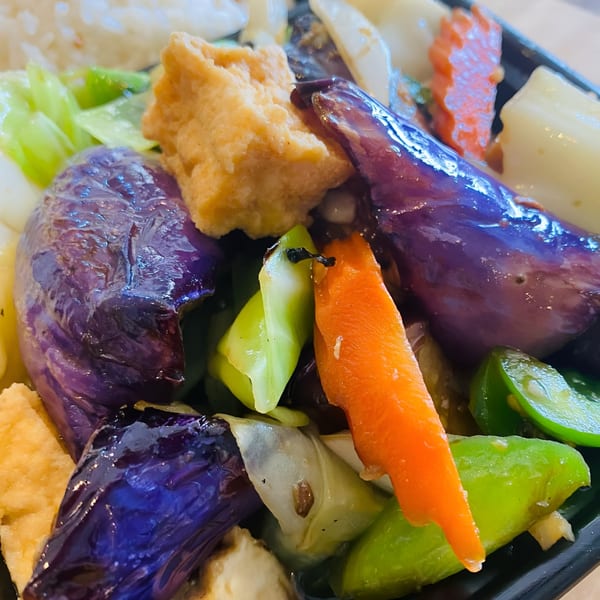 Close-up of a vibrant Thai dish with purple eggplant, orange carrots, green peppers, and fried tofu.