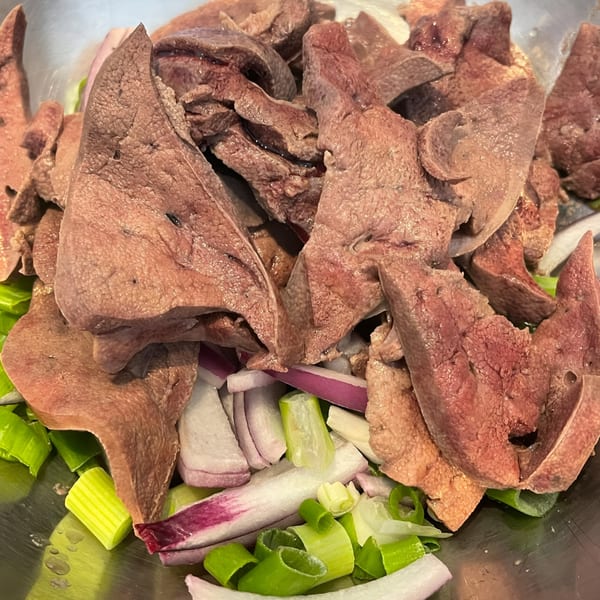 Sliced raw liver, red onions, and green onions in a metal bowl, ready for cooking.