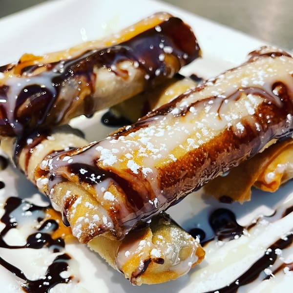 Crispy Thai dessert spring rolls drizzled with chocolate and condensed milk, dusted with powdered sugar.