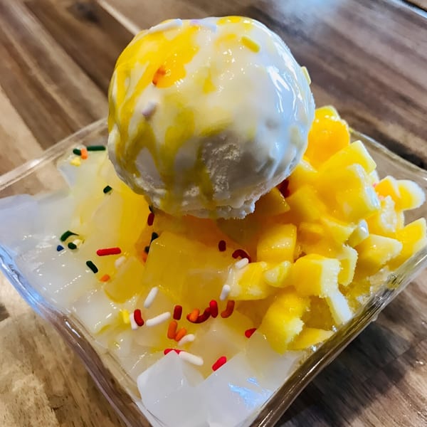 A Thai dessert with a scoop of white ice cream, mango chunks, and colorful sprinkles.